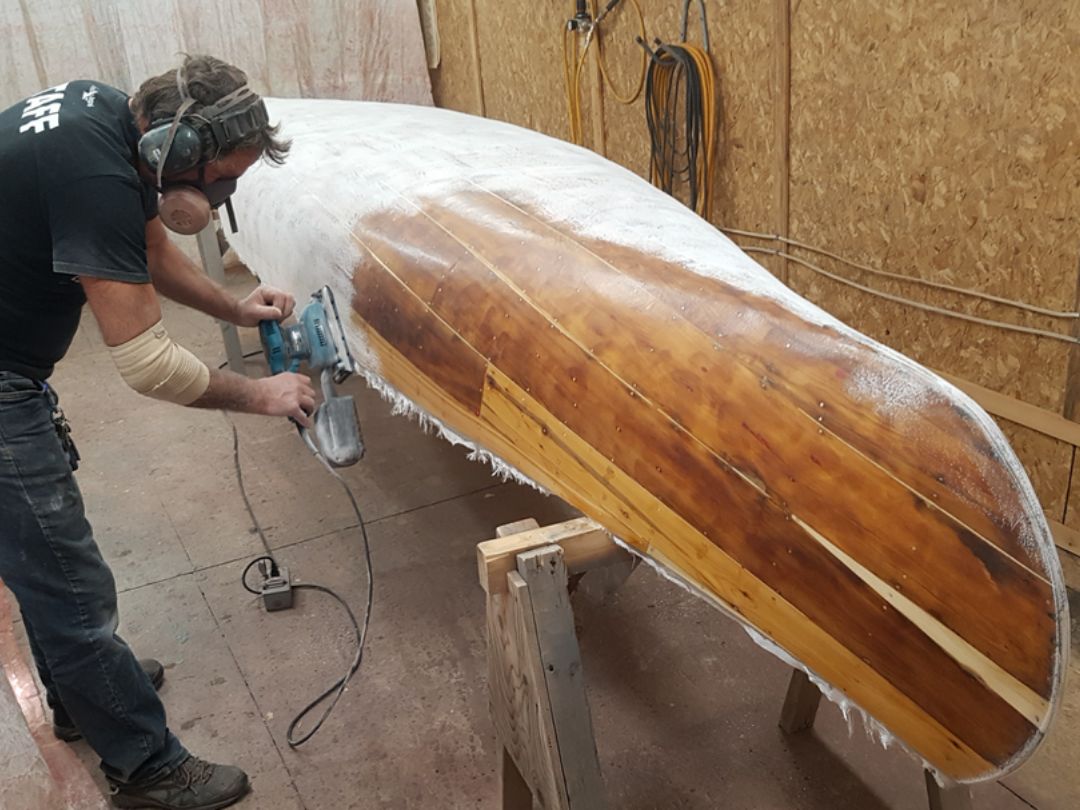 Sablage d'une toile en fibre de verre sur canots en cèdre Expert de Canots Légaré au travail sur une réparation de canot de cèdre